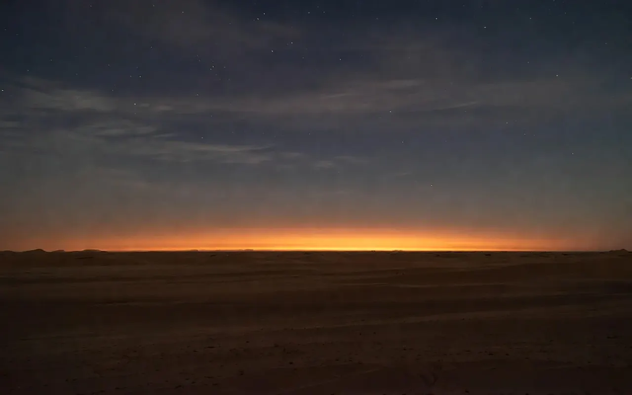 A long flat desert horizon at dusk, a thin ember band of last light under a deep indigo sky with early stars.