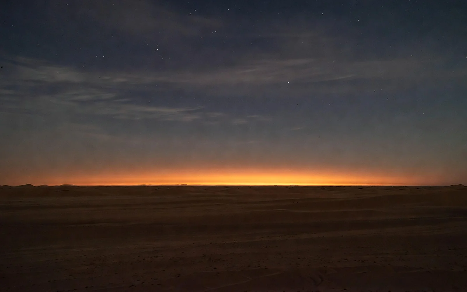 A long flat desert horizon at dusk, a thin ember band of last light under a deep indigo sky with early stars.